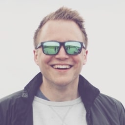 Profile shot of Christian Duncan, wearing a white t-shirt and black collared jacket, alongside a pair of material coloured glasses.